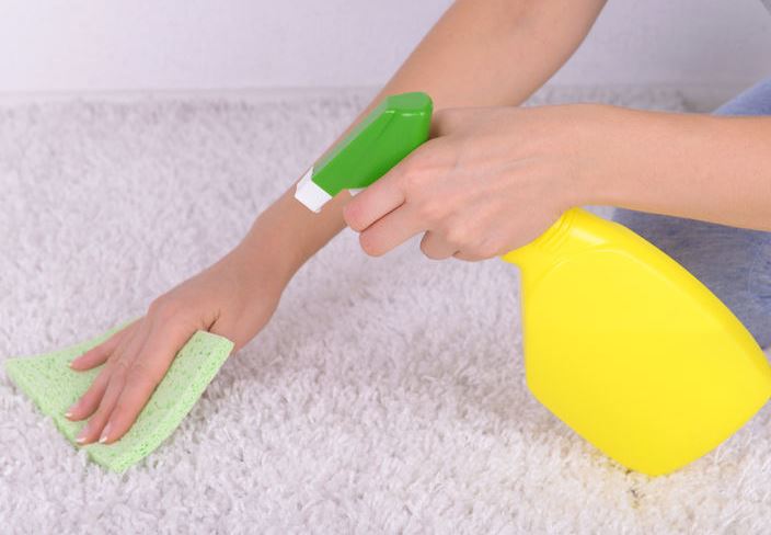 Woman's hand cleaning a white carpet with a spray bottle