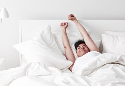 Woman waking up in a bed with white bed linen and pillows